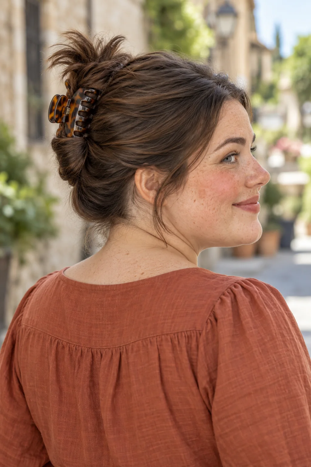 Dark brown hair folded upward into a casual French twist held by a tortoiseshell claw clip with a small fan of ends above it