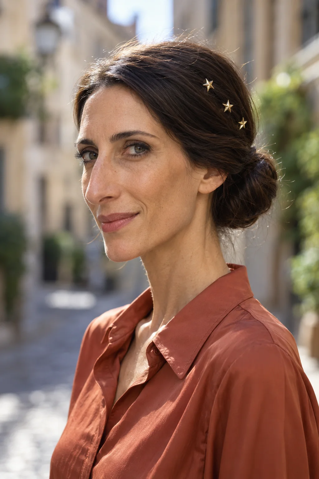Three small gold star pins form a spaced diagonal above one ear on a dark low updo.